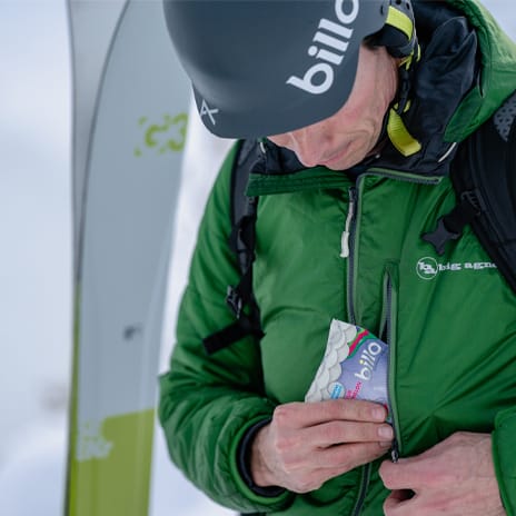 someone who is skiing is putting in his pocket a bag of the billo gummies, it is winter outside